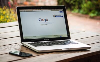 Laptop ouvert sur Google, smartphone à gauche, table en bois, jardin flou