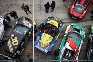 Plusieurs karts de course colorés stationnés au pit stop avec mécaniciens et spectateurs autour
