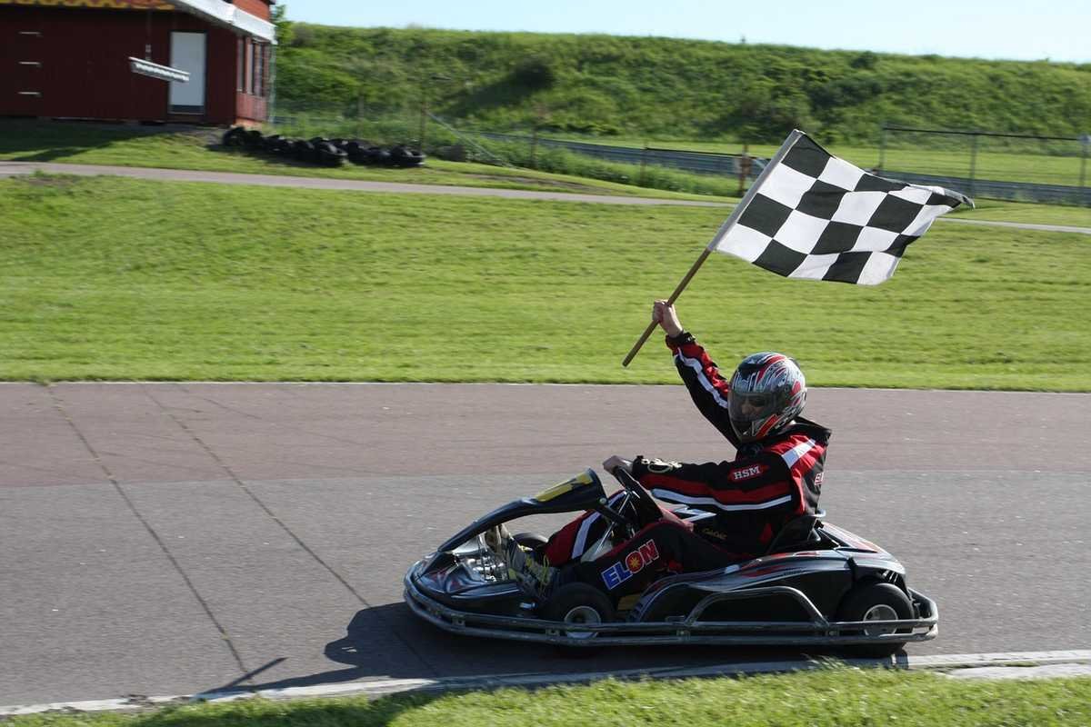 Pilote de karting levant un drapeau à damier à la ligne d'arrivée sur un circuit Pilote de karting levant un drapeau à damier à la ligne d'arrivée sur un circuit