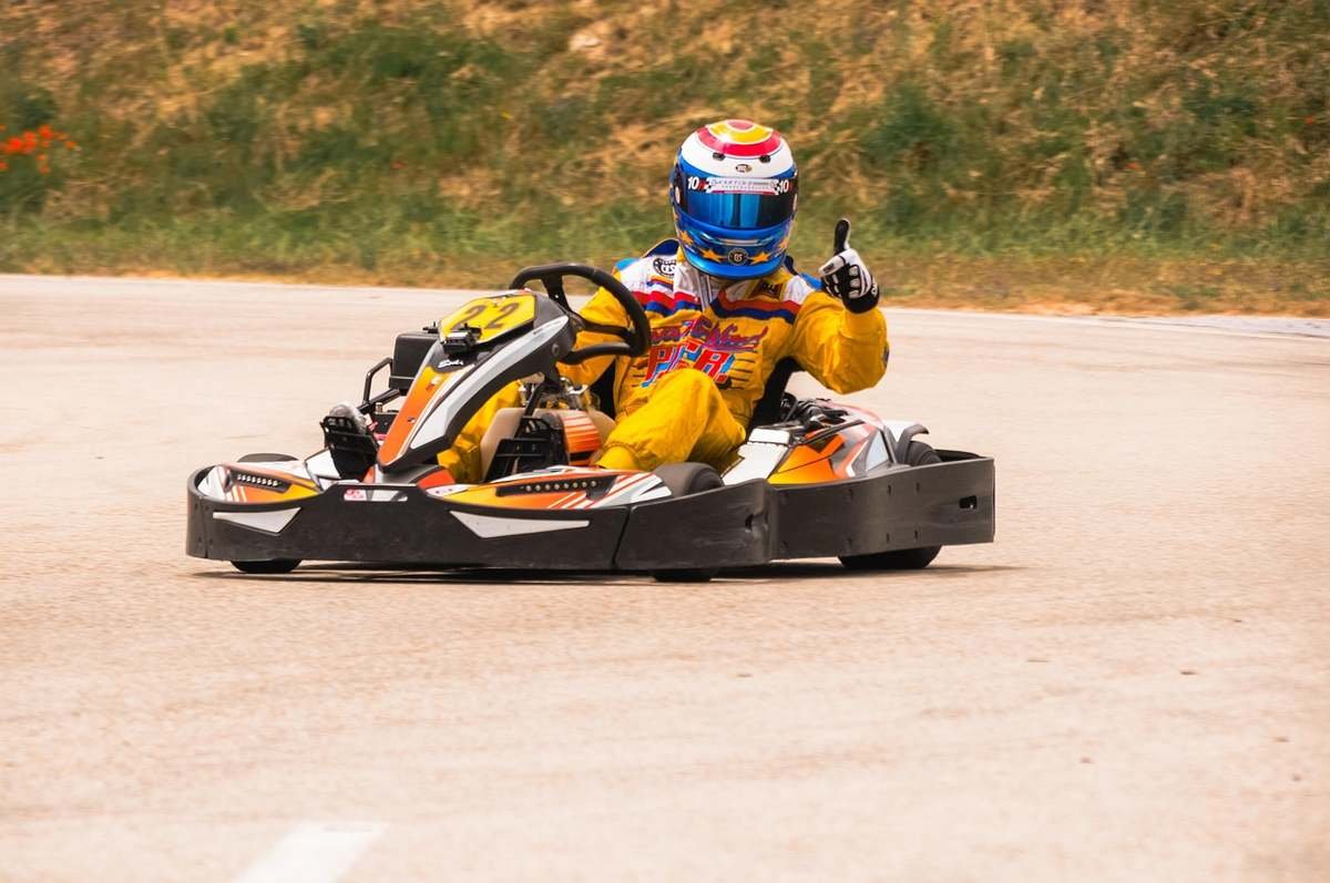 Pilote en combinaison jaune conduisant un kart jaune et orange sur piste asphaltée