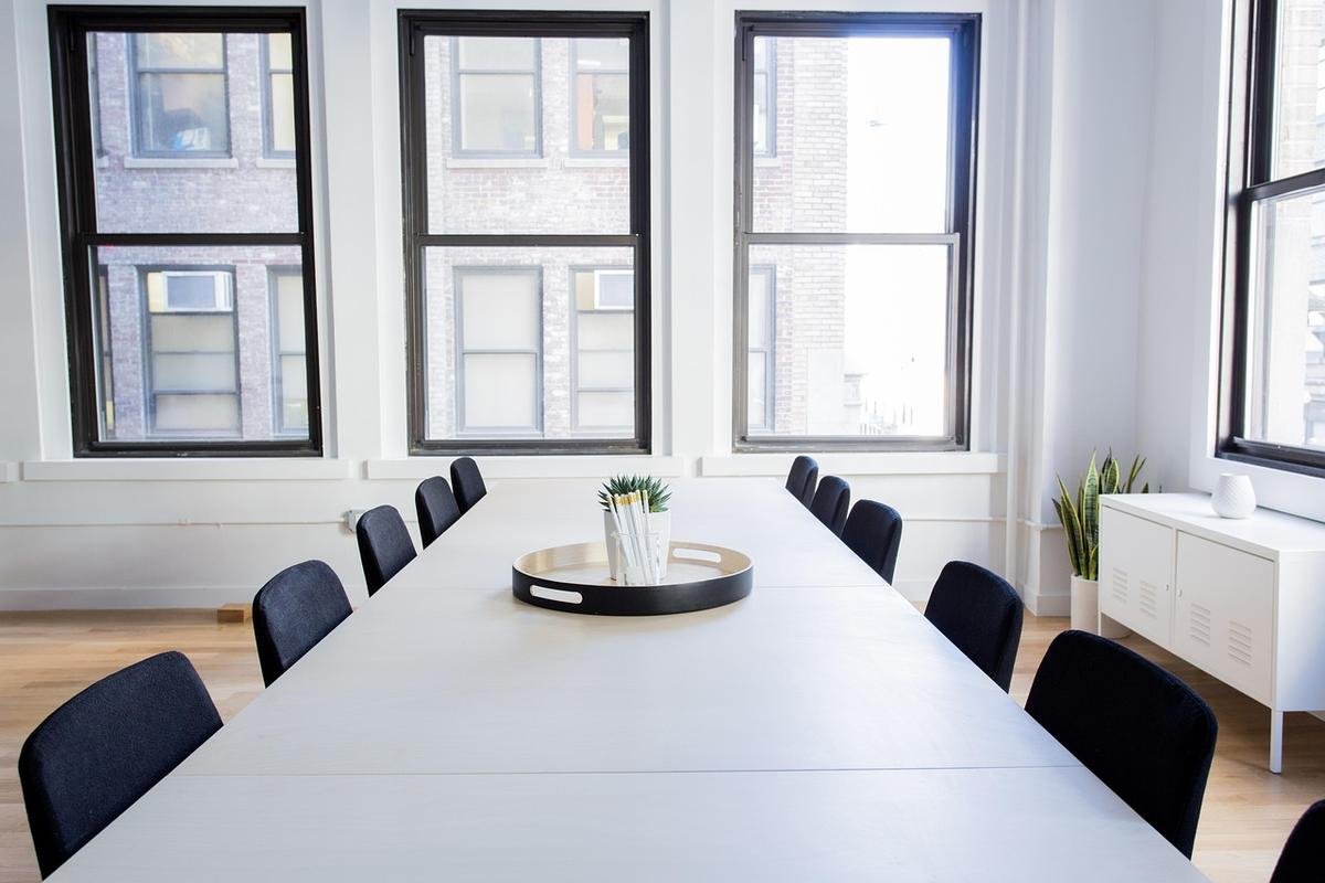 Salle lumineuse avec grande table, chaises noires, fenêtres et petite plante